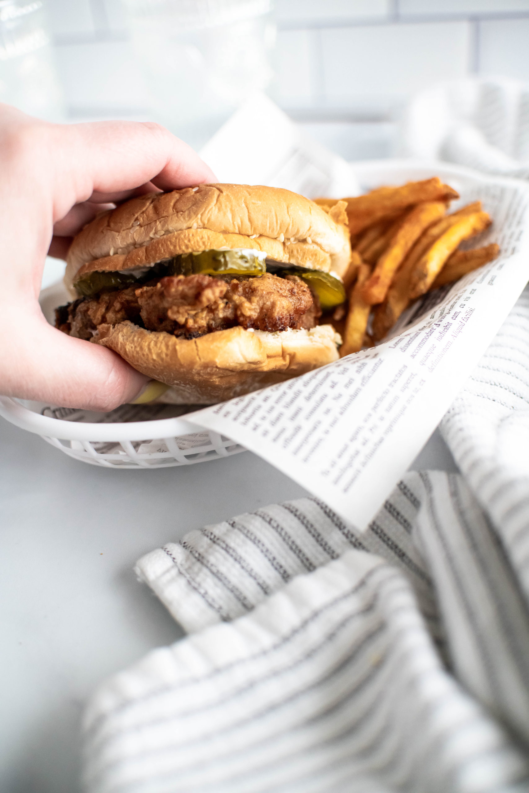 Hand reaching into a white plastic food basket to grab a fried chicken sandwich.