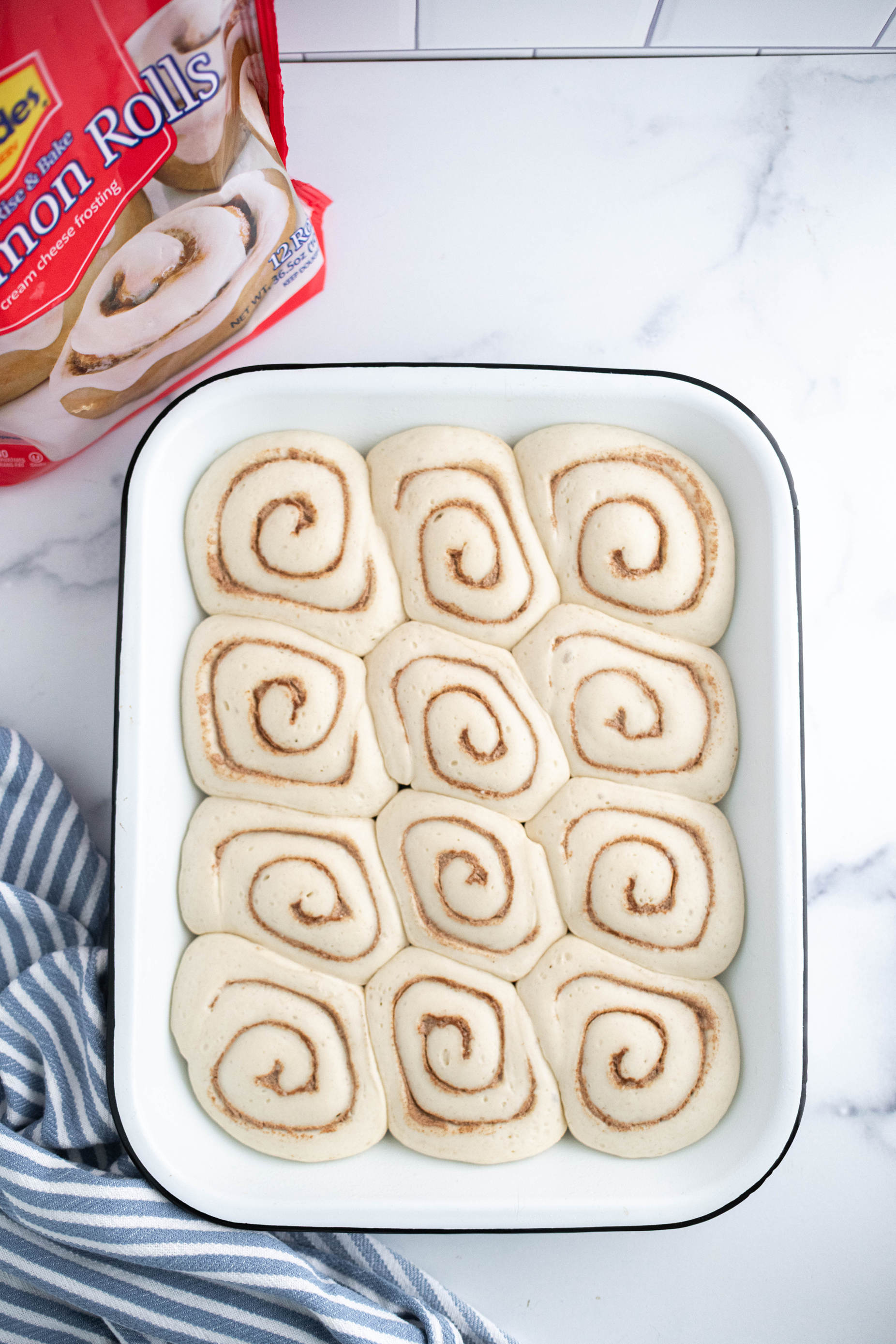 Twelve cinnamon rolls thawed in a white 13 by 9 pan.