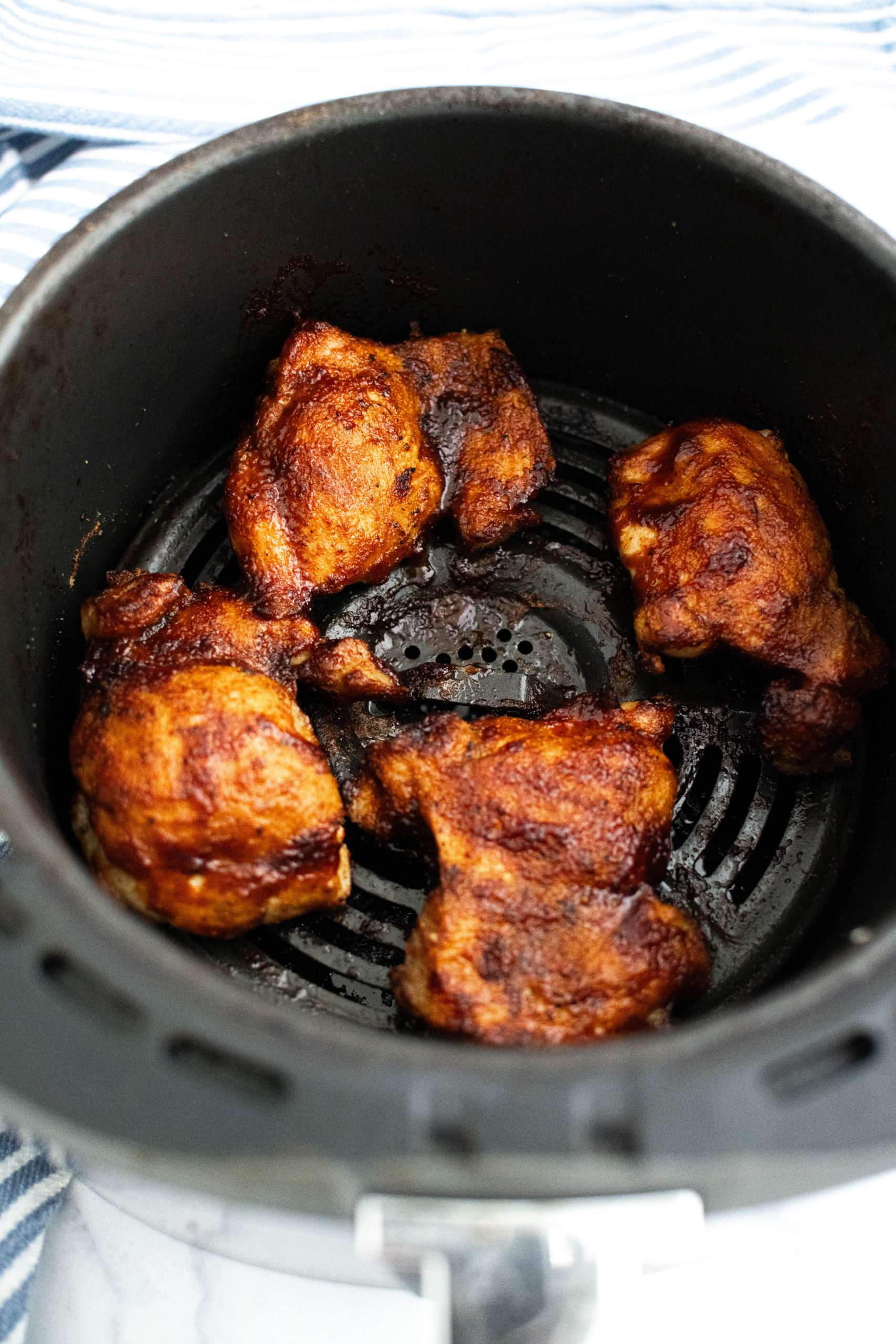 Boneless skinless chicken thighs brushed with barbecue sauce in an air fryer basket.