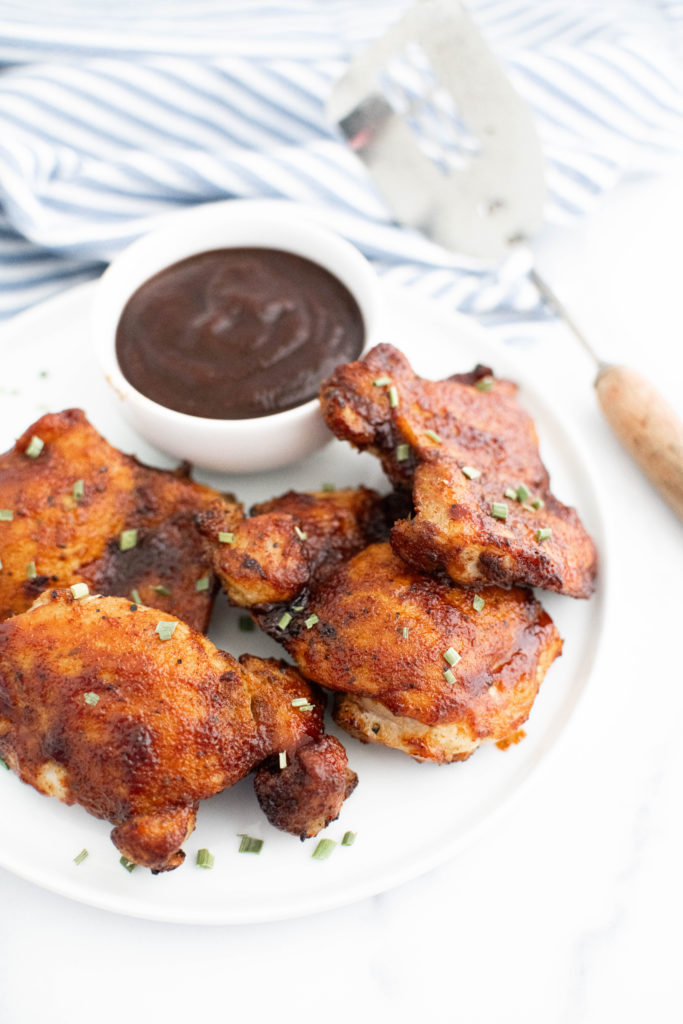 Air fryer barbecue chicken on a round white plate with a small bowl of barbecue sauce on the plate.