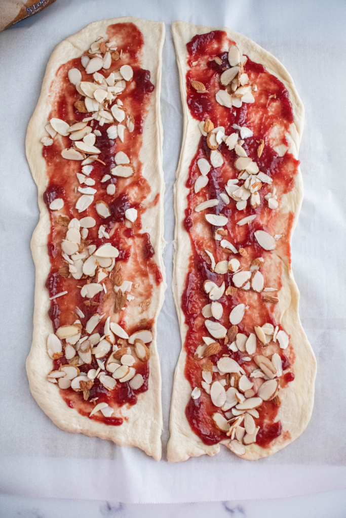 Two rectangular pieces of dough each spread with raspberry preserves and sprinkled with sliced almonds.