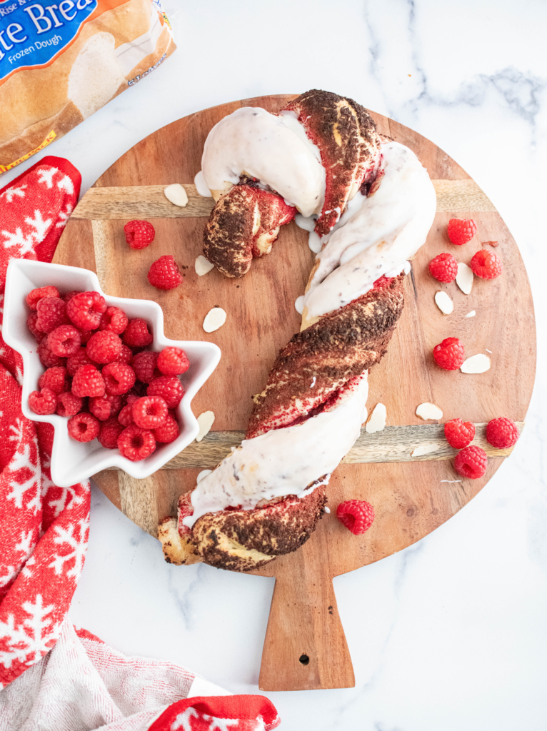 Baked raspberry almond bread twisted into a candy cane shape with one twist covered in freeze dried raspberry crumbs and the other covered in thick white glaze.