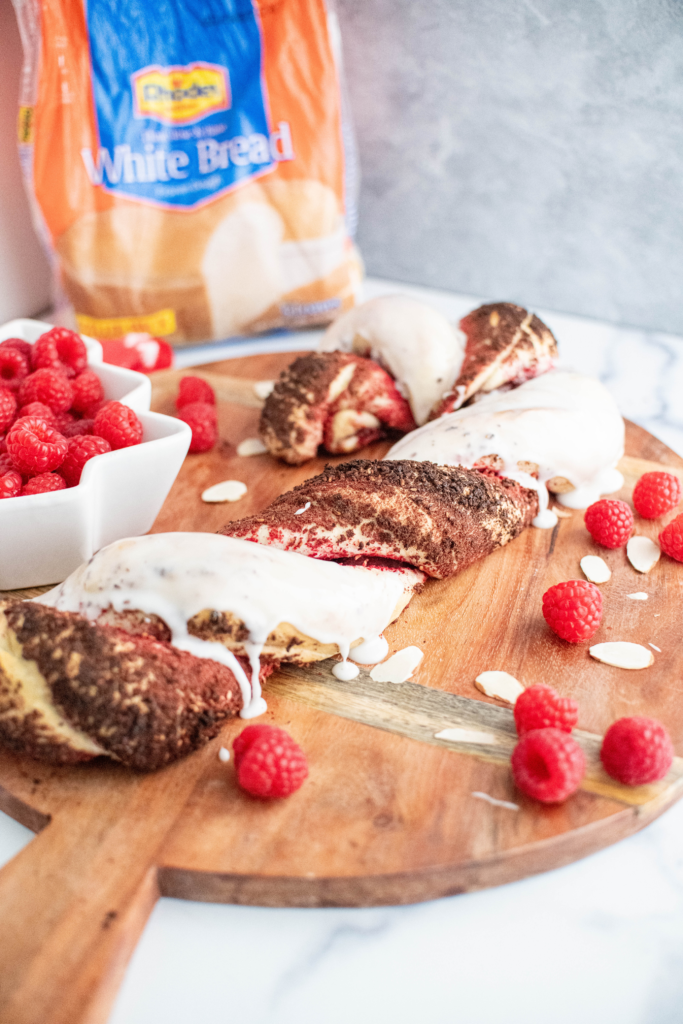 Baked raspberry almond bread twisted into a candy cane shape with one twist covered in freeze dried raspberry crumbs and the other covered in thick white glaze.