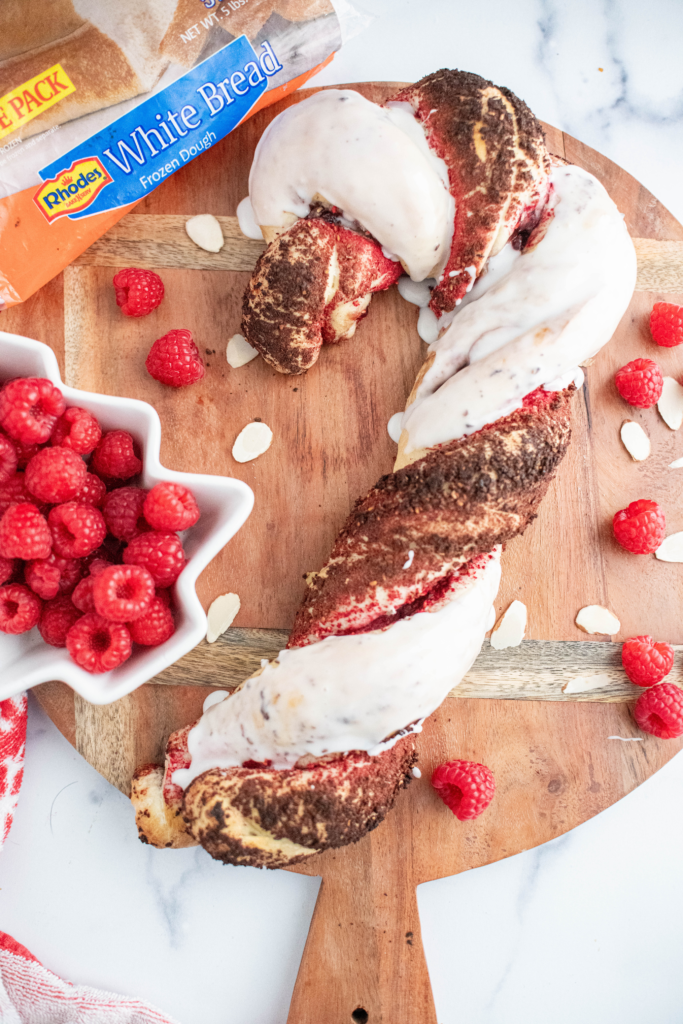 Baked raspberry almond bread twisted into a candy cane shape with one twist covered in freeze dried raspberry crumbs and the other covered in thick white glaze.