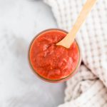 Mason jar filled with pizza sauce with a wooden spoon in the jar.