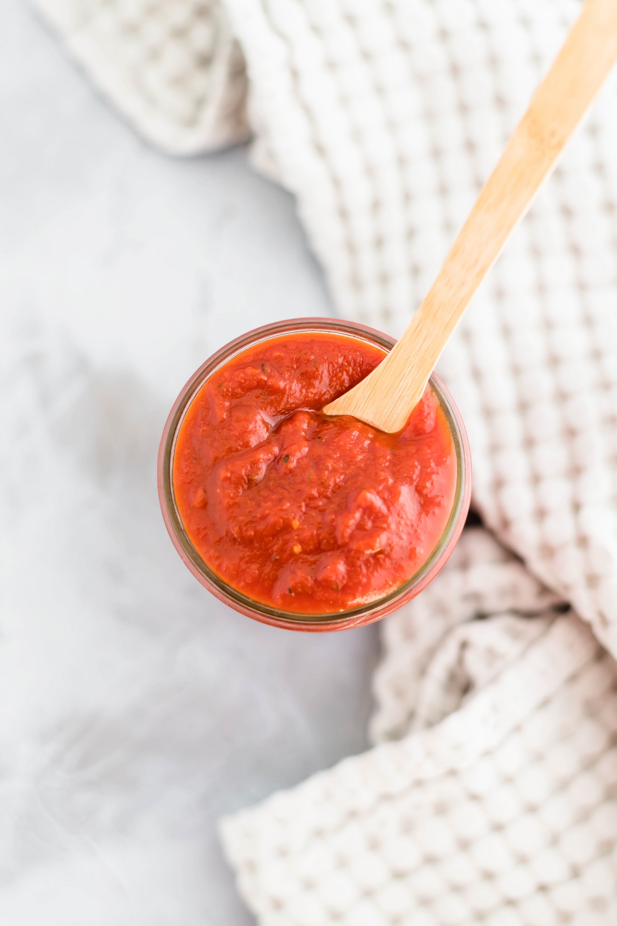 Mason jar filled with pizza sauce with a wooden spoon in the jar.