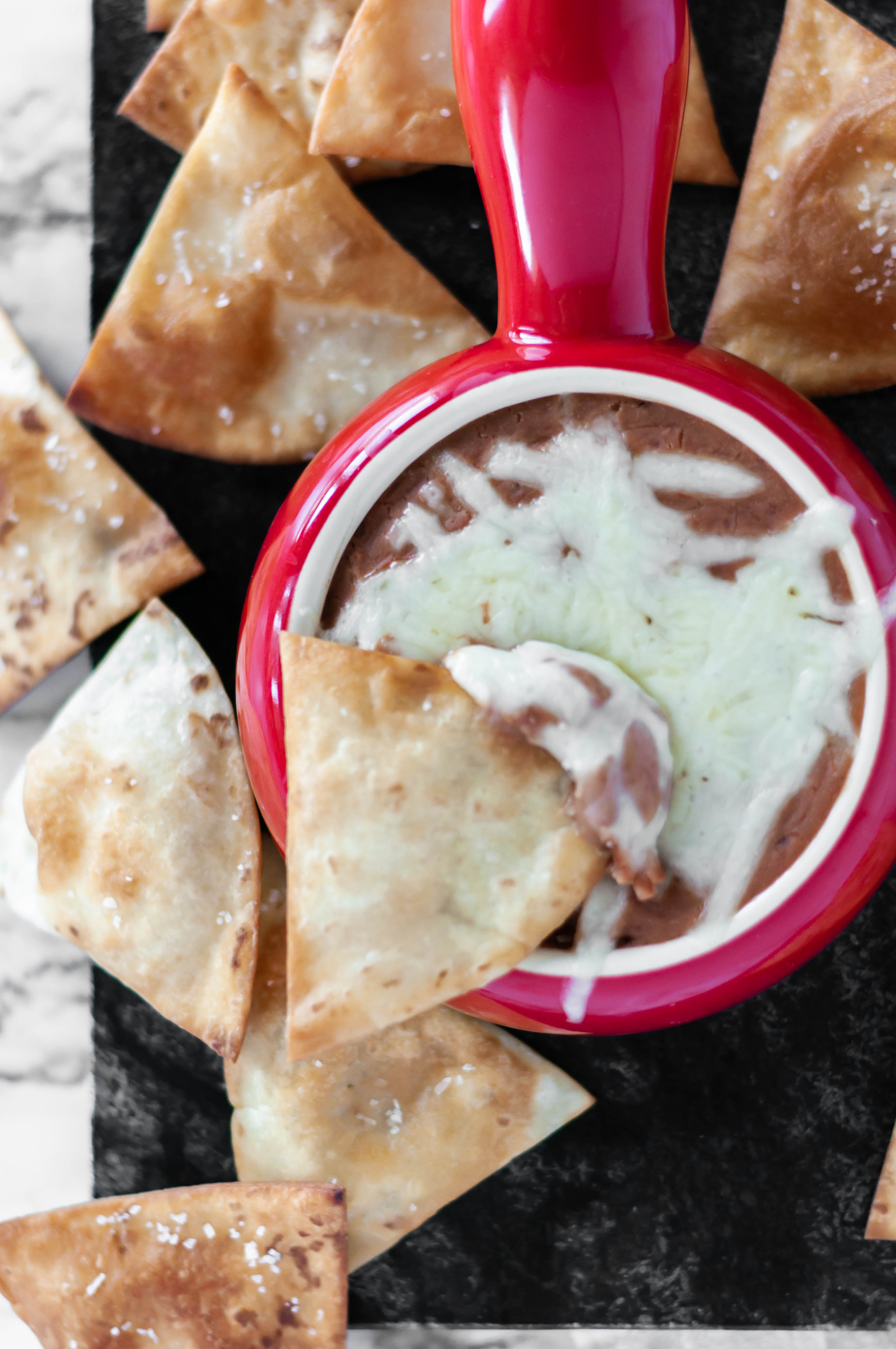 Slow Cooker Cheesy Bean Dip is the perfect addition to your football watch party. 4 ingredients mixed in your slow cooker, a few hours and you're ready for snacking. Homemade flour tortilla chips up your game.