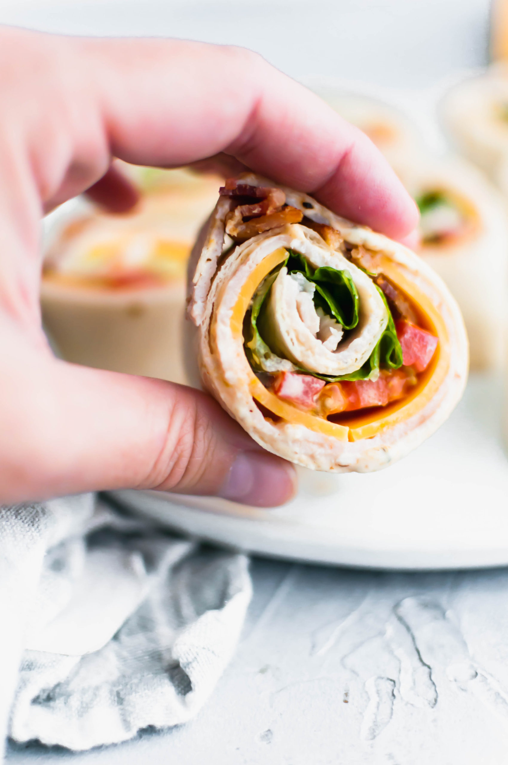 These Turkey Club Pinwheels turn the classic sandwich into a fun, bite-size appetizer. Great for parties or a fun lunch option. Spiced mayo, sharp cheddar cheese, deli turkey, bacon, lettuce and tomato make up these delicious pinwheels.