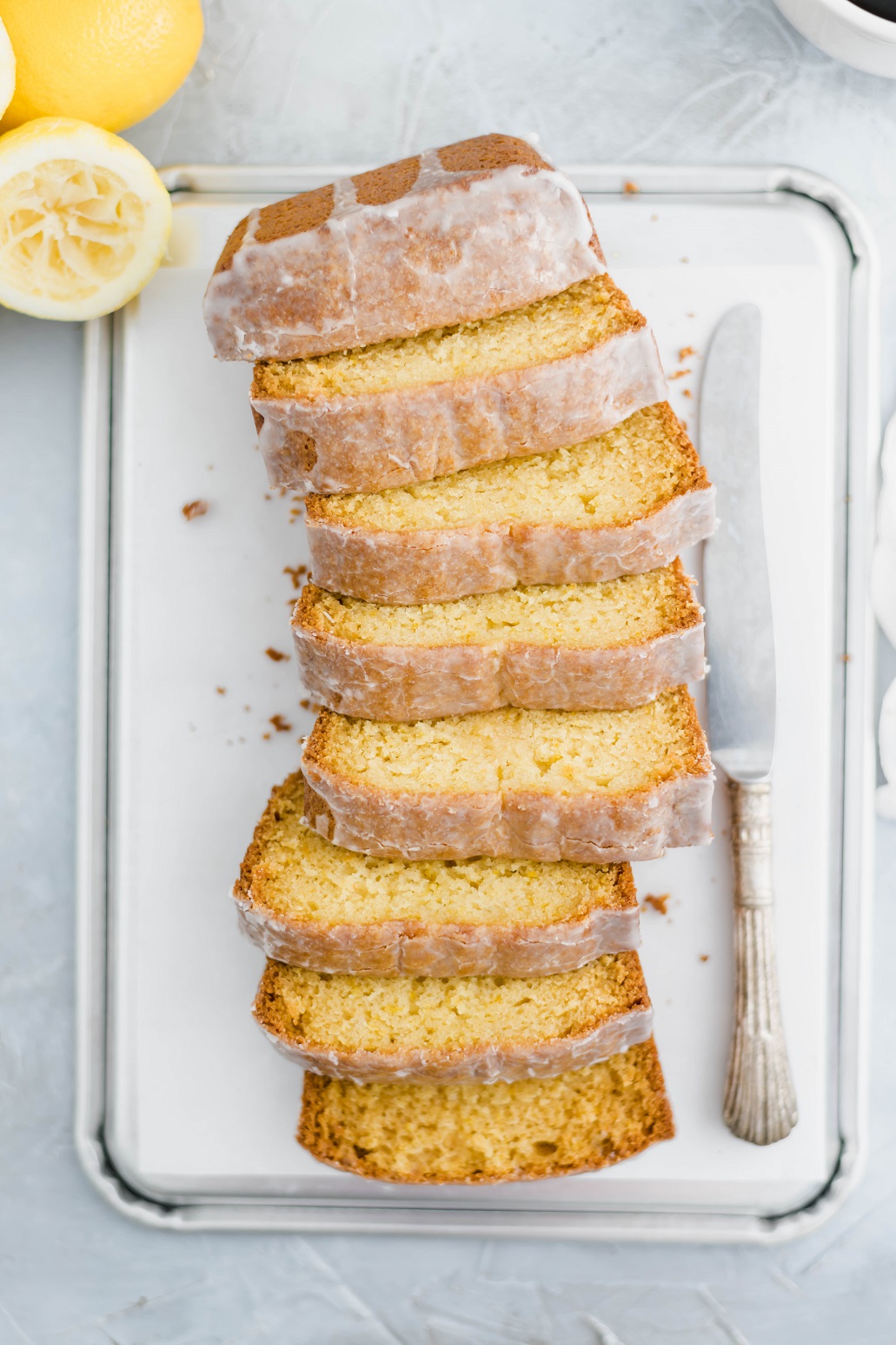 Sliced Starbucks lemon loaf arranged in a slight s shape with a decorative knife to the right and squeeze lemons in the top left corner.