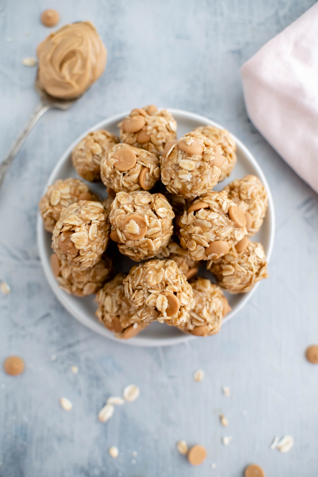 White bowl filled with no bake peanut butter balls. Spoon of peanut butter in background.