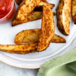 Air fryer potato wedges on a gray plate with a small glass bowl of ketchup on the left side of the plate.
