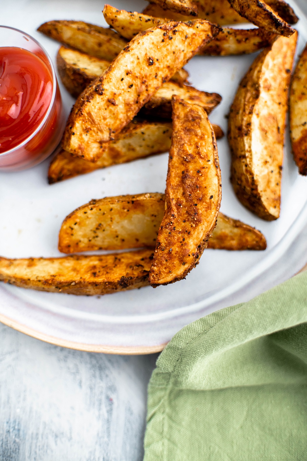 Air fryer potato wedges on a gray plate with a small glass bowl of ketchup on the left side of the plate.