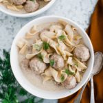 Two bowls of swedish meatball soup garnished with fresh dill. Two spoons to the right side.