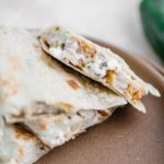 Sliced jalapeno popper quesadilla on a clay colored plate, exposing the inside of the quesadilla. Jalapeno in the background.