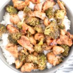 Bowl of white rice topped with sheet pan sweet chili chicken and broccoli with a spoon in the bowl.