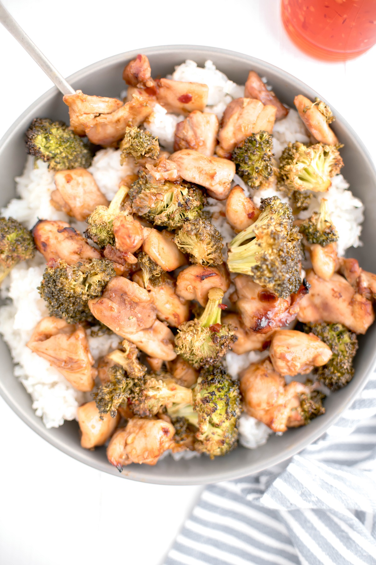 Bowl of white rice topped with sheet pan sweet chili chicken and broccoli with a spoon in the bowl.