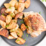 Baked chicken and potatoes on a round gray plate with sprigs of parsley in the upper right corner.