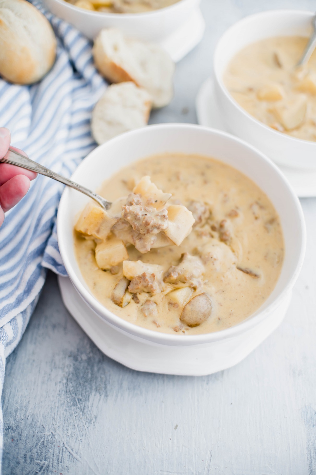 White bowl of cheeseburger soup with a spoonful being lifted out of the bowl.