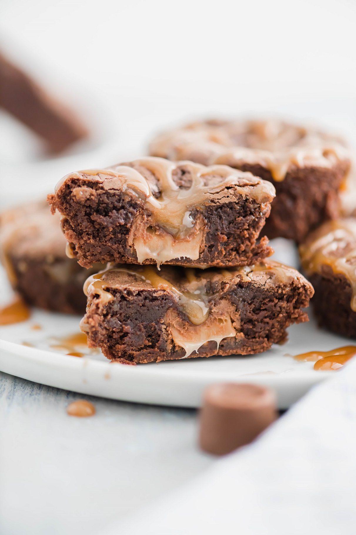 Individual rolo brownie sliced in half to show melted rolo inside. Set on a white round plate with more brownie bites in the background.