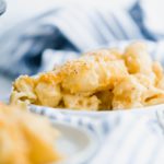 Scoop of skillet mac and cheese on a small white round plate. Plate resting on a blue and white striped cloth napkin.