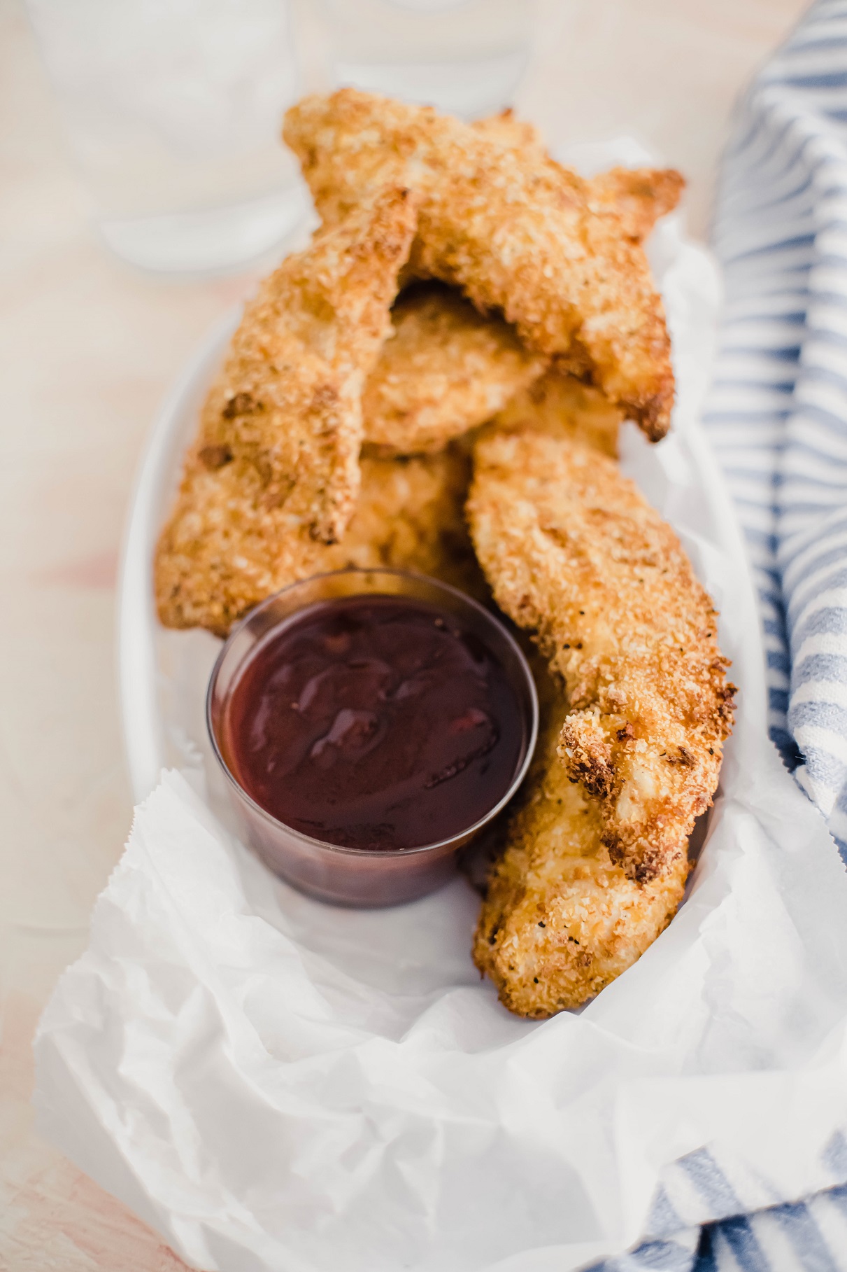 White plastic food basket with parchment paper, filled with air fryer chicken tenders and a small glass bowl of barbecue sauce.