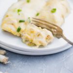 Plate of cream cheese chicken enchiladas with a fork cutting a bite.