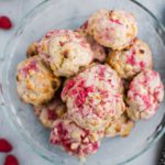 Raspberry and White Chocolate Scones piled in a glass pie plate surrounded by fresh raspberries.