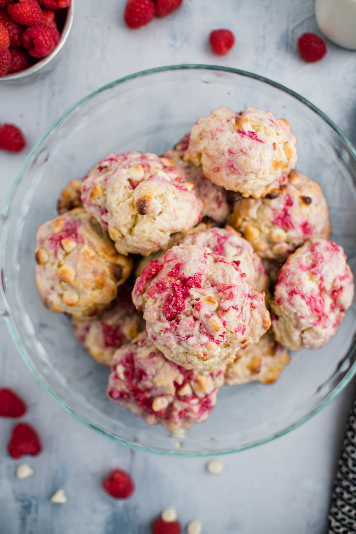 Raspberry and White Chocolate Scones piled in a glass pie plate surrounded by fresh raspberries.