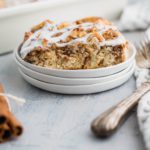 Slice of cinnamon roll casserole on a small white plate with casserole dish in the background.