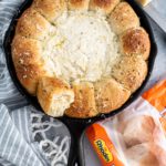 Cast iron skillet with rolls around the exterior and white pizza dip in the center.