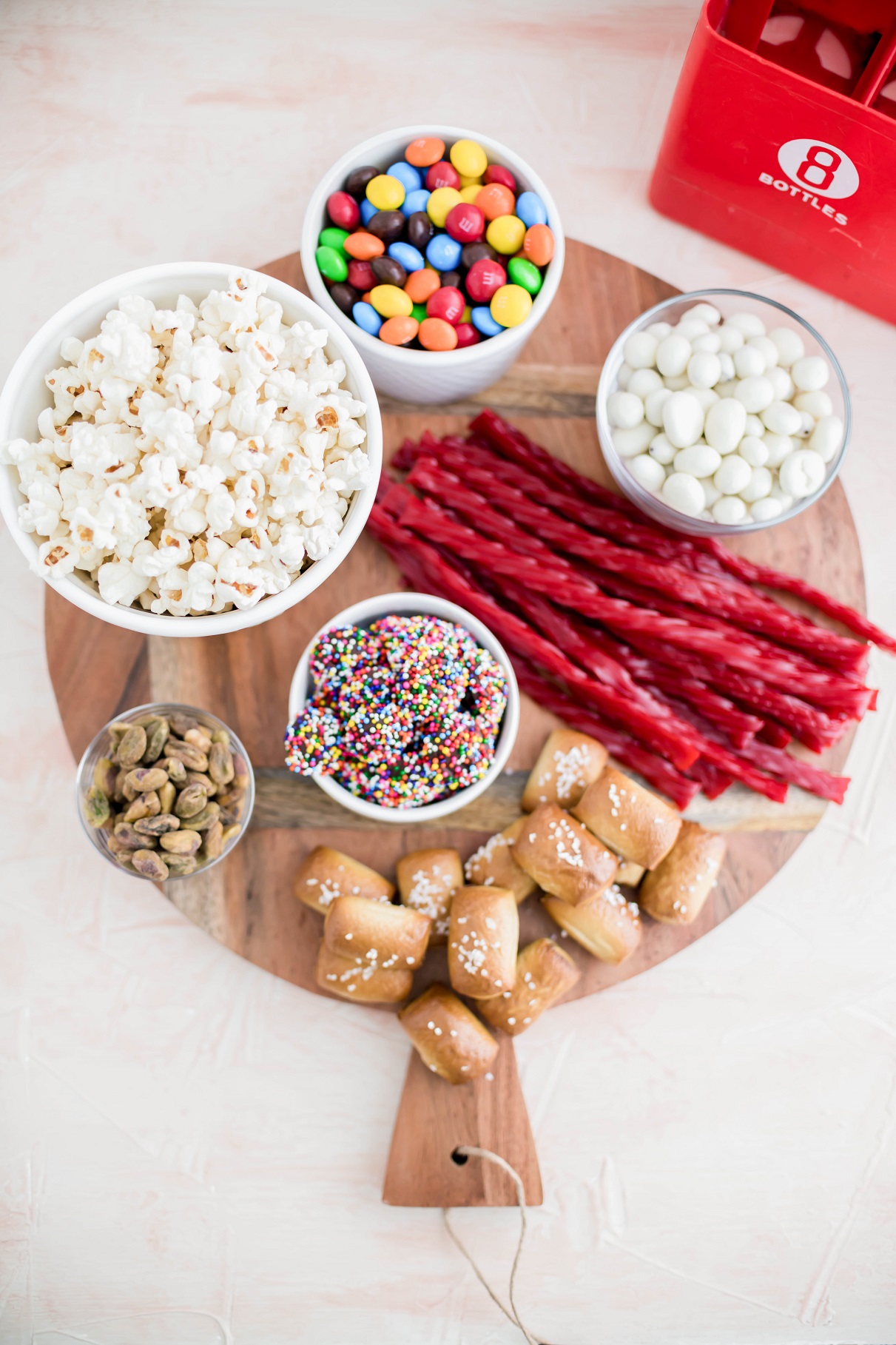 Wooden board filled with soft pretzels, candy, popcorn and nights for a movie night snack board.
