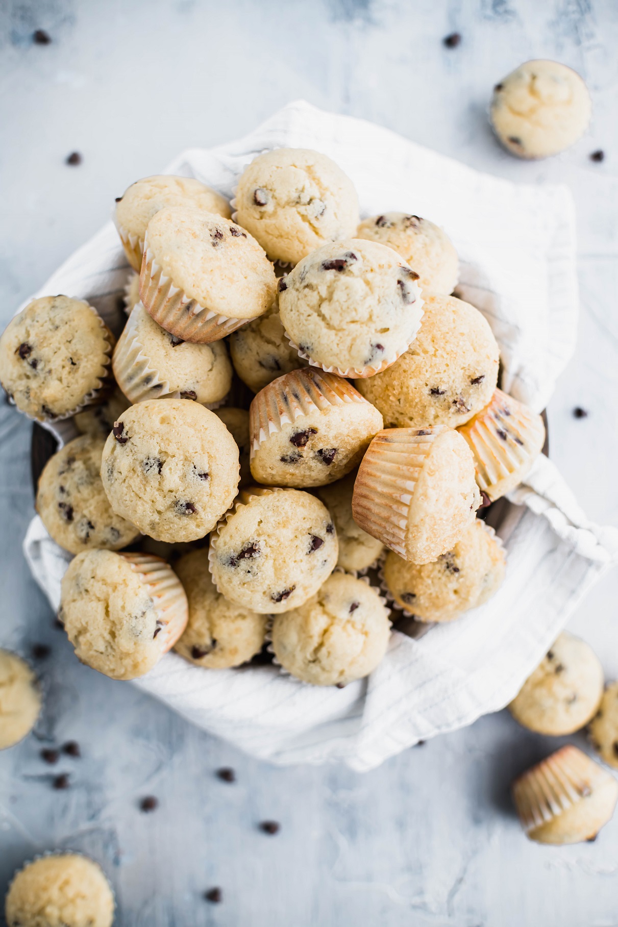 Bowl lined with a white and gray striped towel piled high with mini chocolate chip muffins.