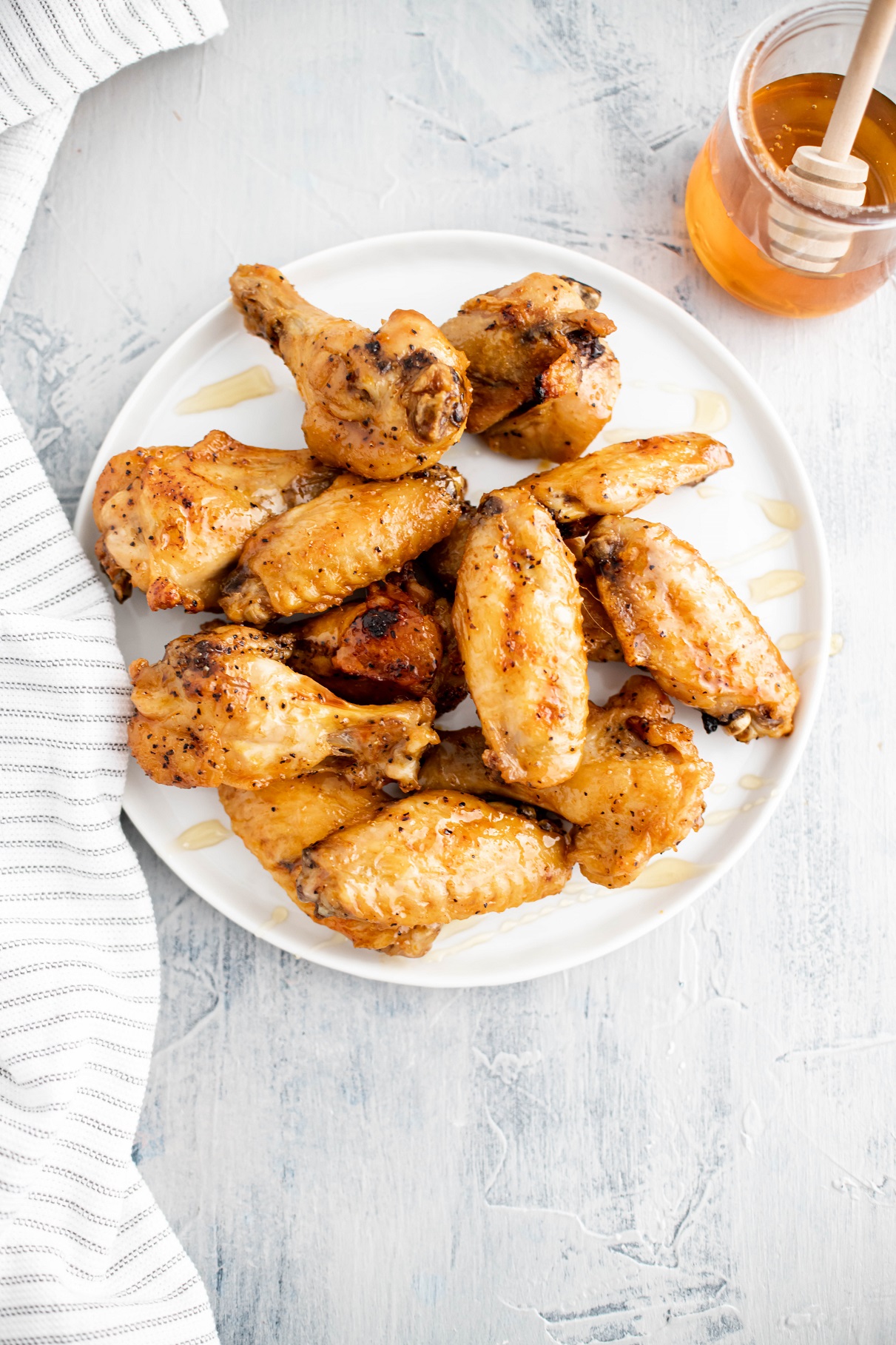 White round plate piled with hot honey wings. Glass jar of honey with a dipper in the background.