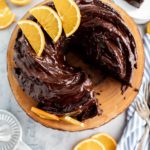 Orange Chocolate Bundt Cake on a wooden cake stand with a slice cut out and on a plate in the background.