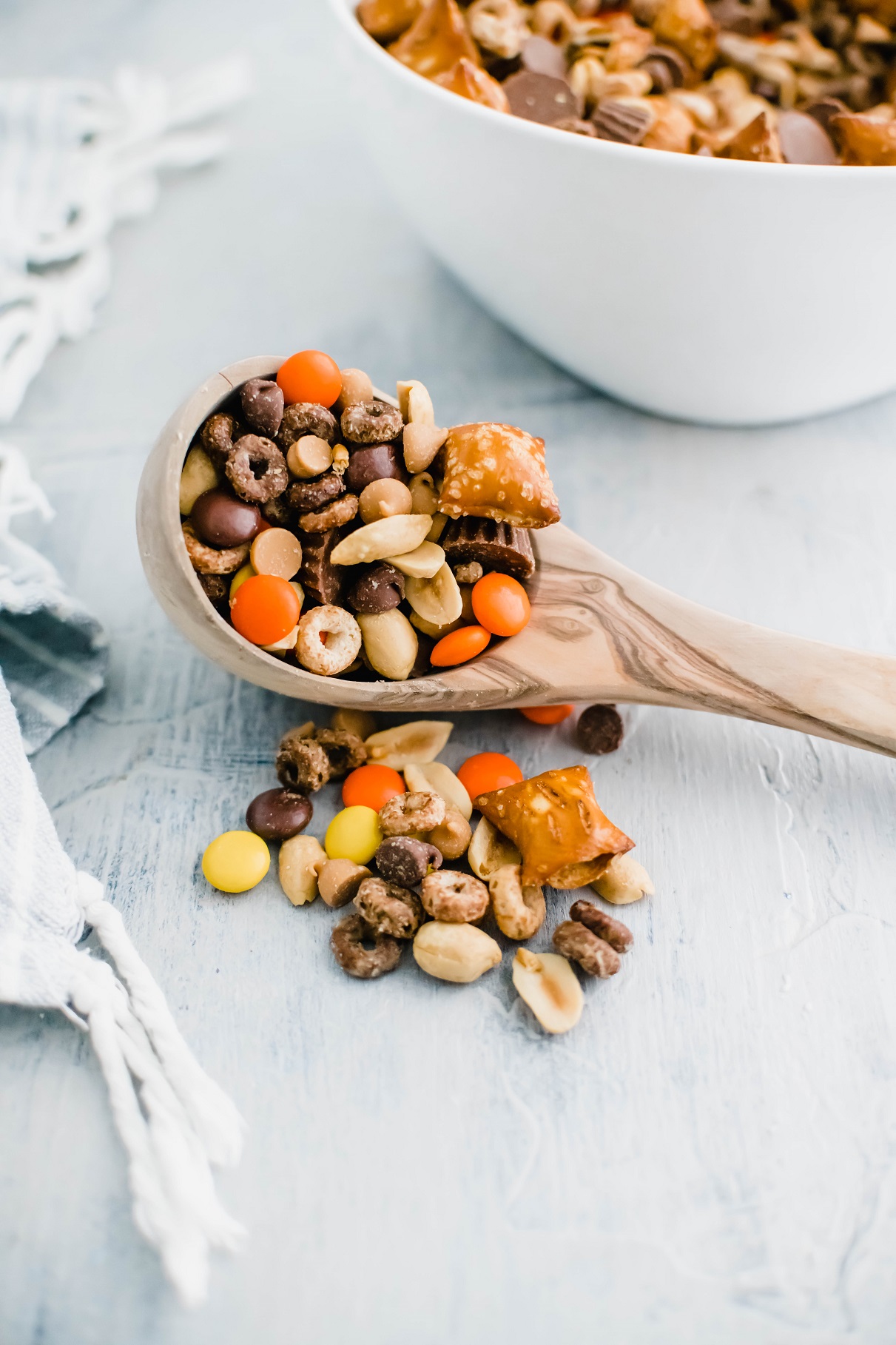 Wooden ladle filled and overflowing with peanut butter trail mix with a white bowl of trail mix in the background.
