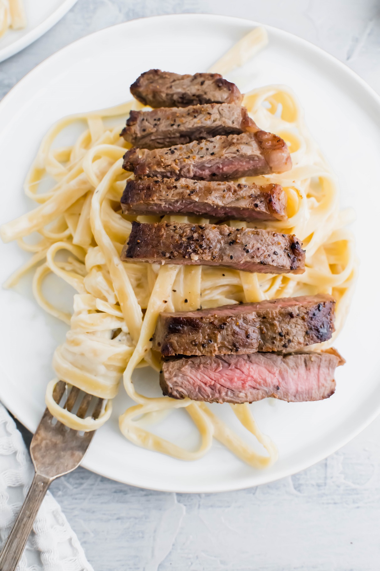 Fettucine alfredo on a plate topped with sliced steak.