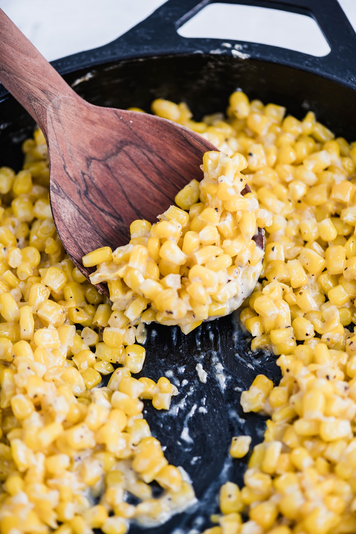 Honey butter corn in a cast iron skillet with a wooden spoon scooping out some.
