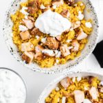 Two bowl of tumeric rice topped with grilled chicken shawarma, tzatziki dip and crumbled feta.