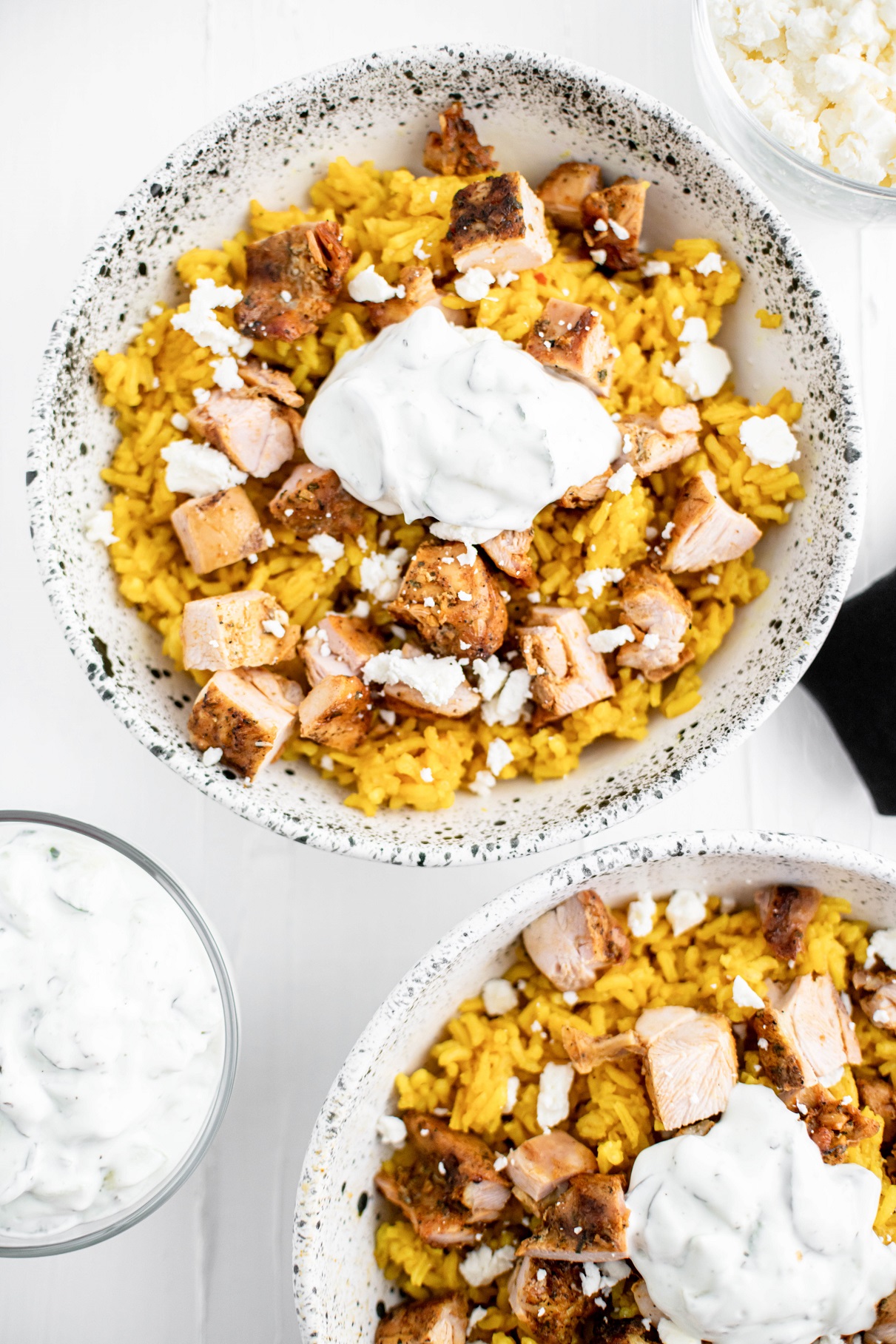 Two bowl of tumeric rice topped with grilled chicken shawarma, tzatziki dip and crumbled feta.