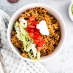 Bowl of cheesy rice with beef topped with shredded lettuce, diced tomatoes and sour cream.