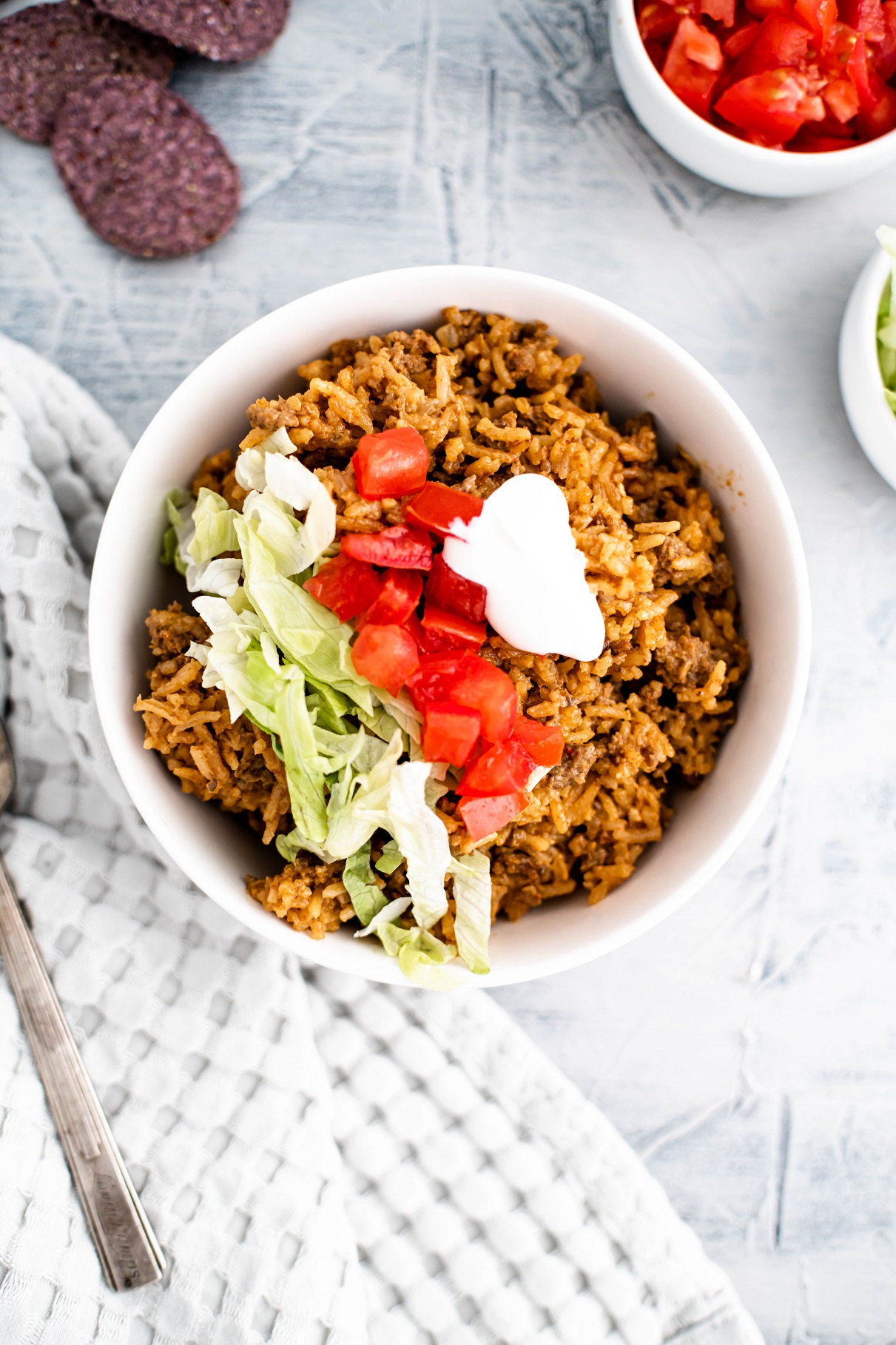 Bowl of cheesy rice with beef topped with shredded lettuce, diced tomatoes and sour cream.