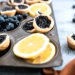 Mini blueberry pies in an antique muffin pan with slices of lemon in some of the spots.