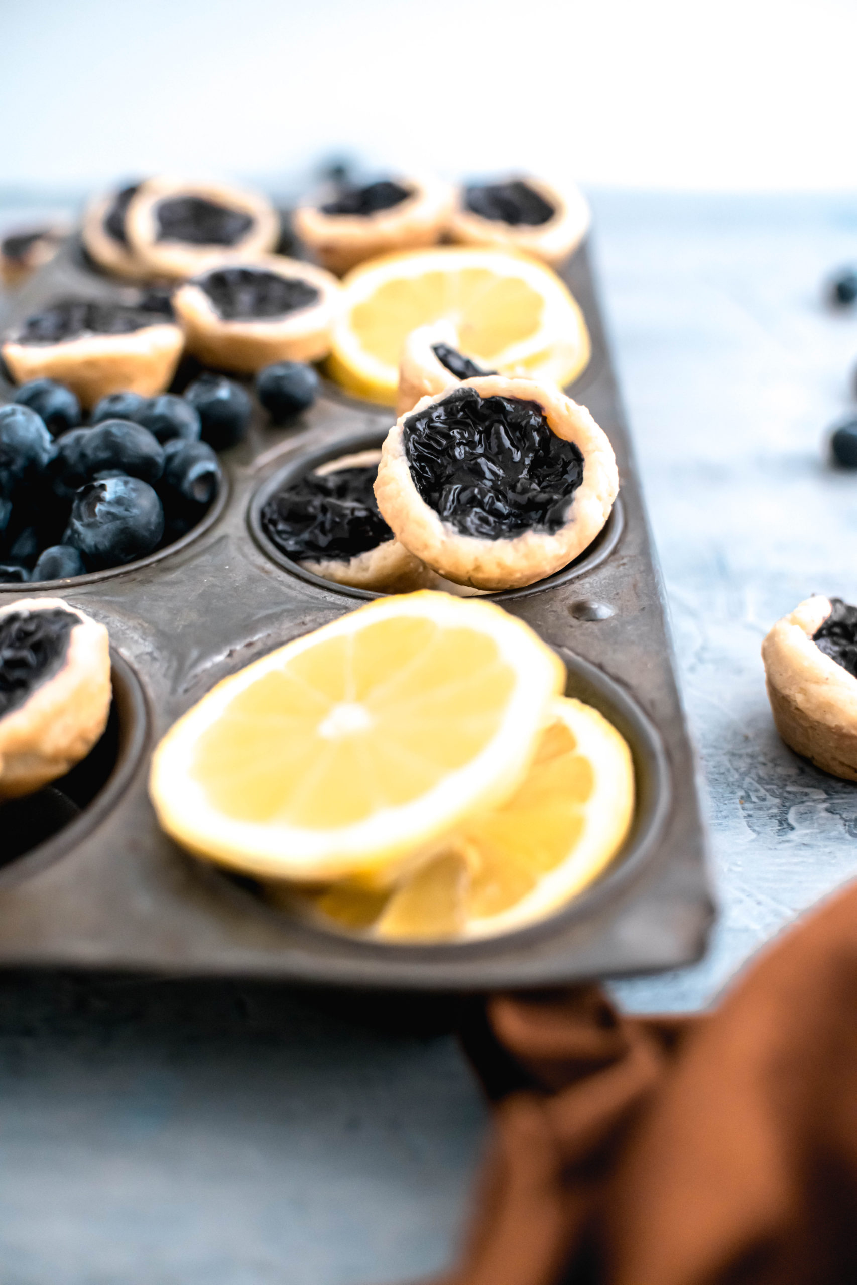 Mini blueberry pies in an antique muffin pan with slices of lemon in some of the spots.