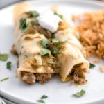 Two turkey enchiladas on a round white plate with a side of Mexican rice.