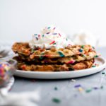 Stack of three funfetti waffles with whipped cream on top.