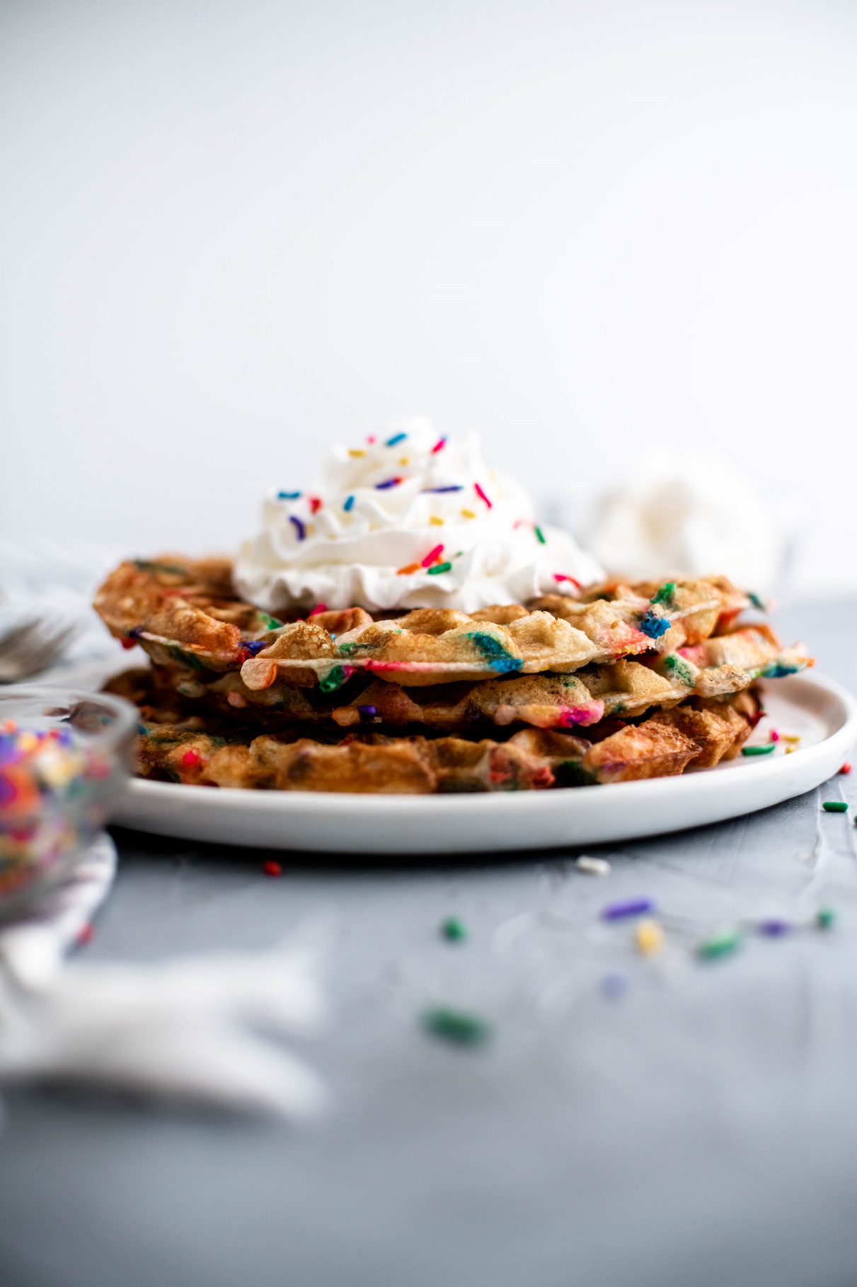 Stack of three funfetti waffles with whipped cream on top.