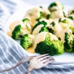White round plate with fresh steamed broccoli drizzled with cheese sauce.