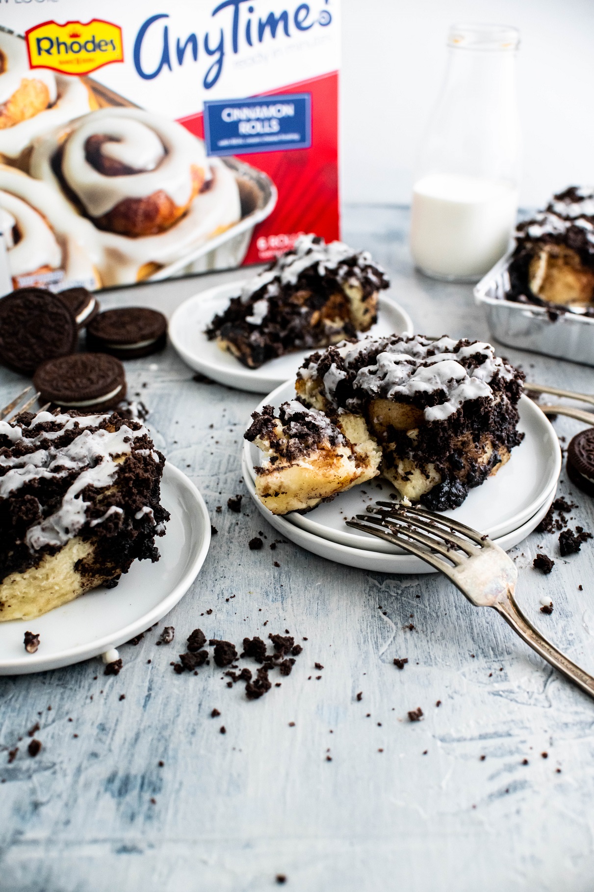 Three small white round plates with a cookies and cream cinnamon roll on each. Rhodes packaging in the background.