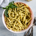 Corkscrew pasta covered in creamy pesto in a pale pink bowl.