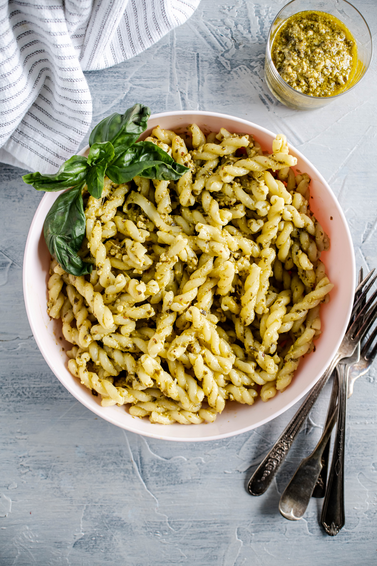 Corkscrew pasta covered in creamy pesto in a pale pink bowl.